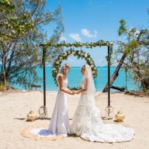 A couple getting married on the beach at Villa Paradise Cove Airlie Beach, with the aqua blue water in the background, and white sand in the foreground
