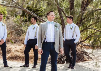 Groom and groomsmen standing on beach by tree at Paradise Cove Resort in the Whitsundays