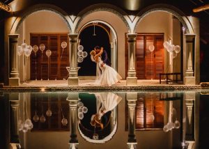 Bride and groom sharing a romantic evening kiss under the arches at Villa Paradise Cove, Airlie Beach Whitsundays, reflected in the pool surrounded by soft candlelight and balloons.